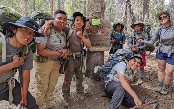 a group of students laugh while posing for a photo on a backpacking course